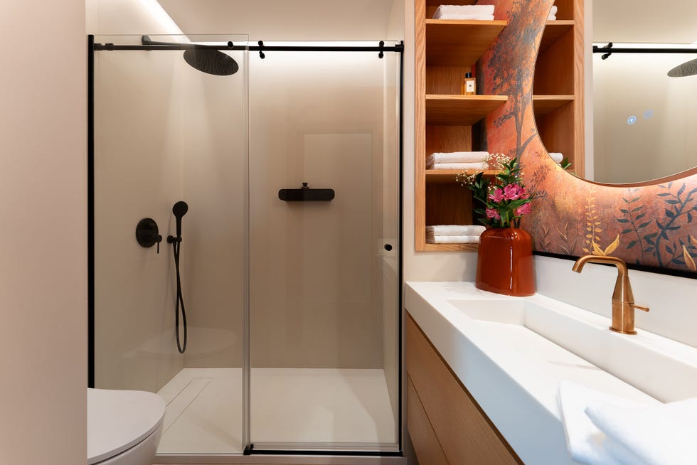 baño con ducha, papel pintado con motivos vegetales y espejo redondo