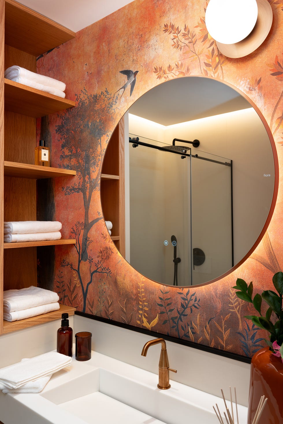 baño con papel pintado con motivos vegetales y espejo redondo