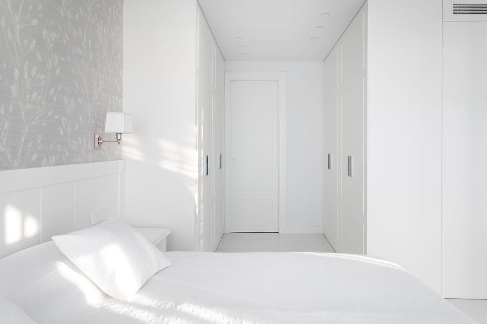 dormitorio con muebles blancos y papel pintado floral en la pared del cabecero