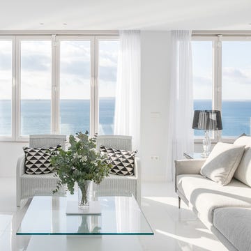 salón con suelo de mármol, mesa de cristal, sofá gris, dos butacas y mueble de tv blanco