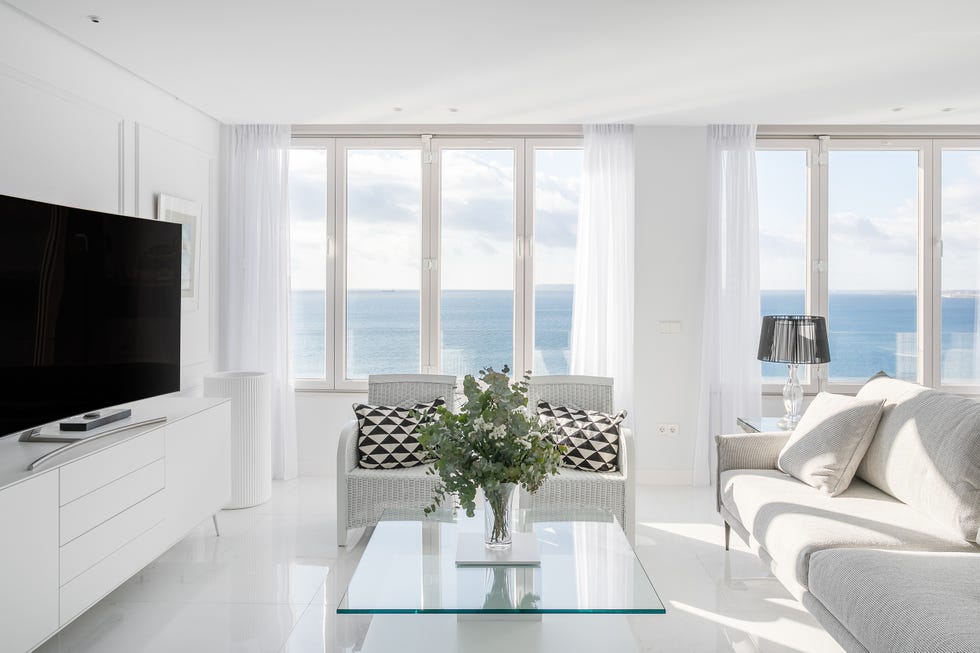 salón con suelo de mármol, mesa de cristal, sofá gris, dos butacas y mueble de tv blanco
