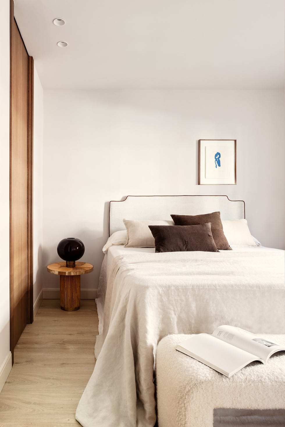 cama con cabecero tapizado en blanco y mesita de noche redonda de madera