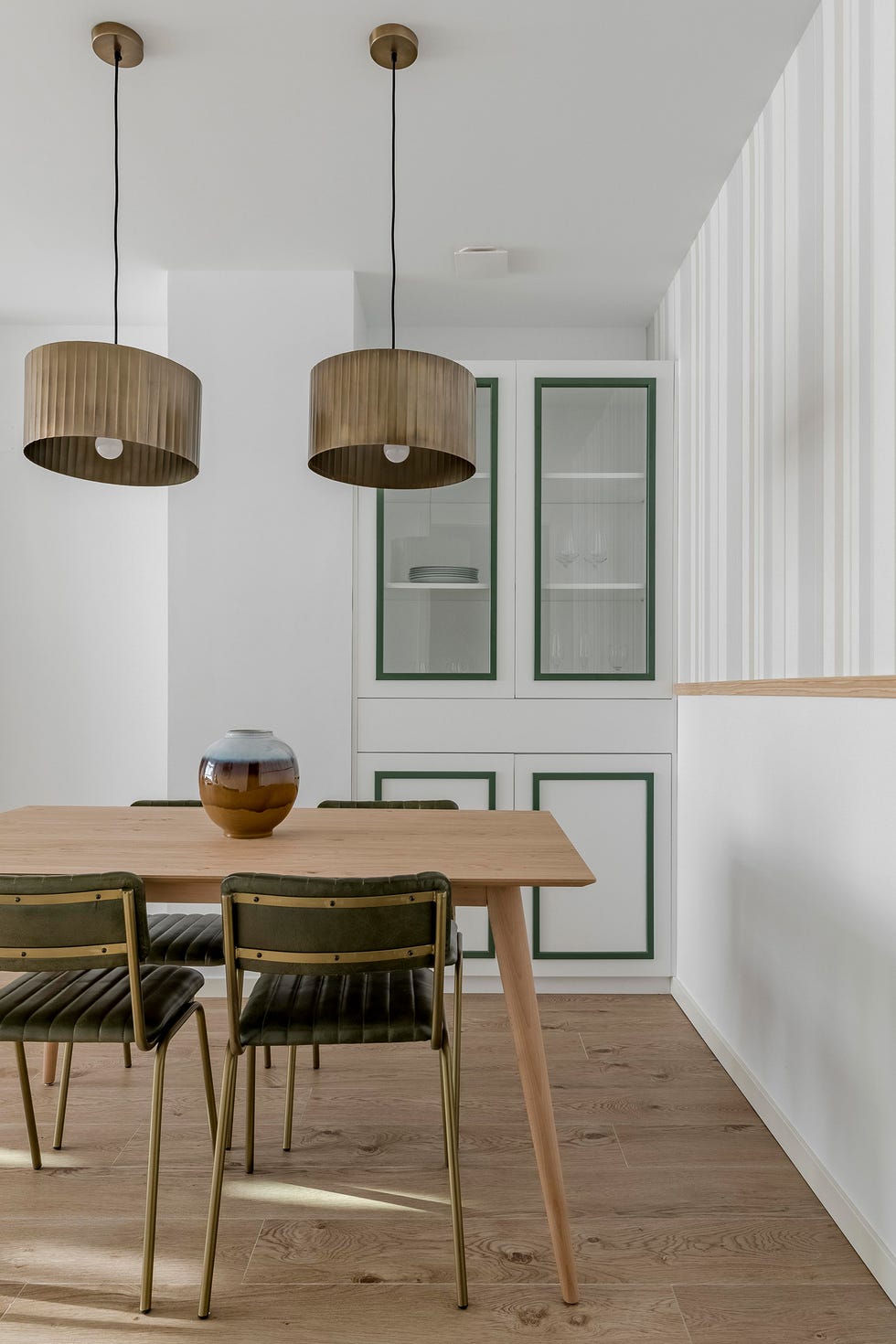 mesa de comedor de madera, sillas de terciopelo verde y vitrina blanca