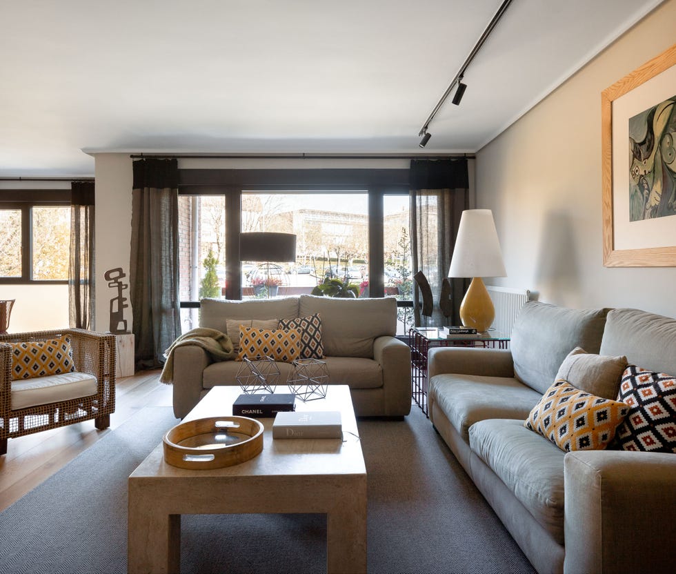 salón moderno con sofás grises, butaca de ratán y mesa de centro de mármol