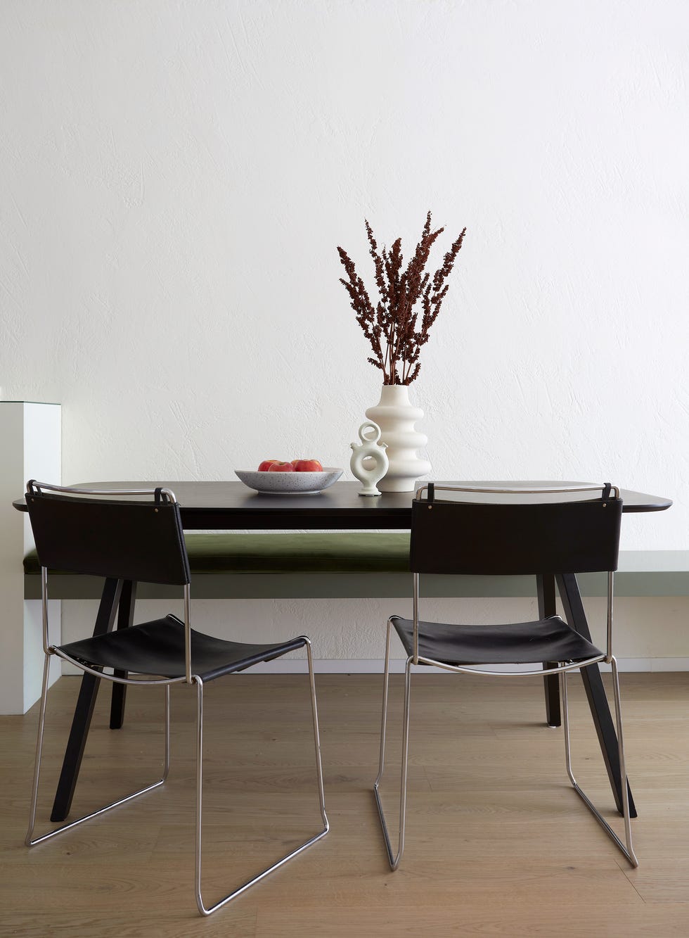 mesa de comedor negra con sillas de piel negra y banco con cojín de terciopelo verde