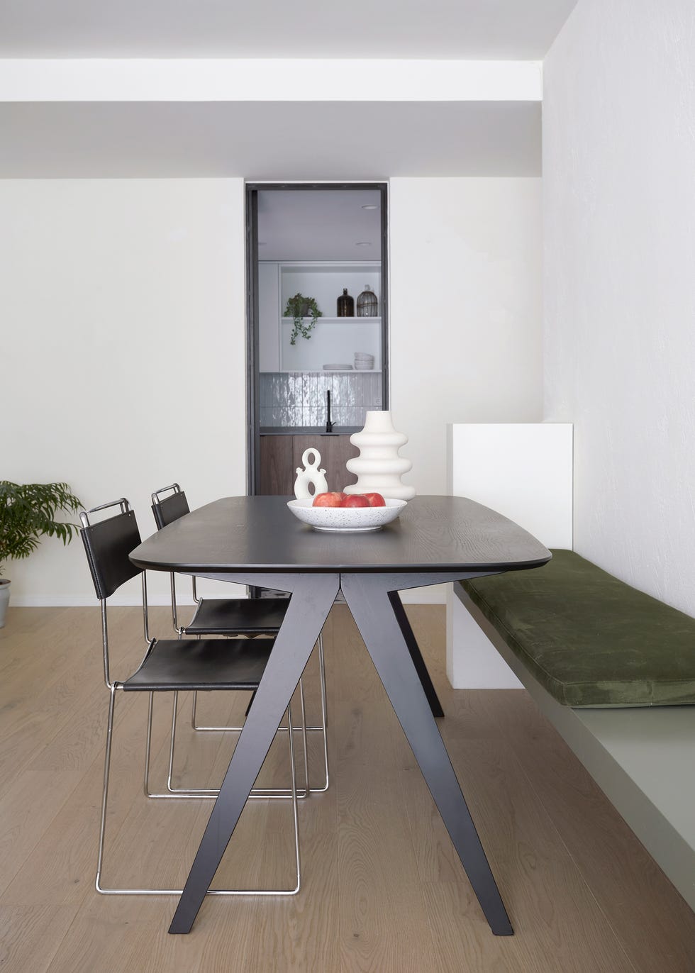 mesa de comedor negra con sillas de piel negra y banco con cojín de terciopelo verde