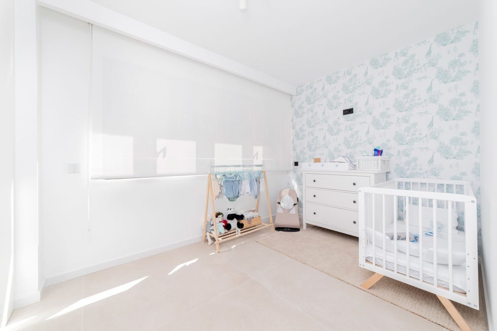 habitación infantil con cuna y cómoda blancas y papel pintado en tonos azules