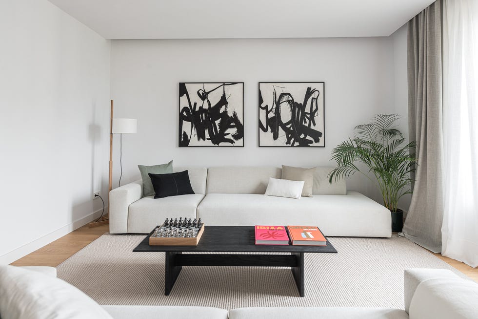 sofás blancos, mesa de centro negra y dos cuadros abstractos