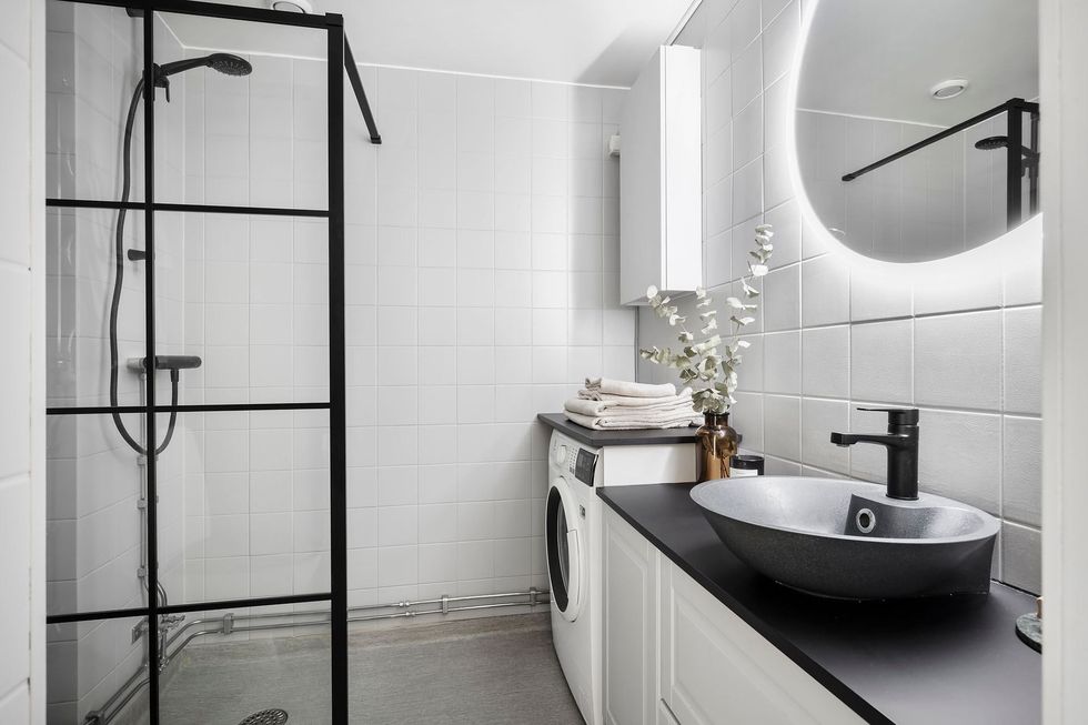 baño moderno con ducha a ras de suelo y mampara francesa, azulejos blancos, espejo redondo y encimera negra