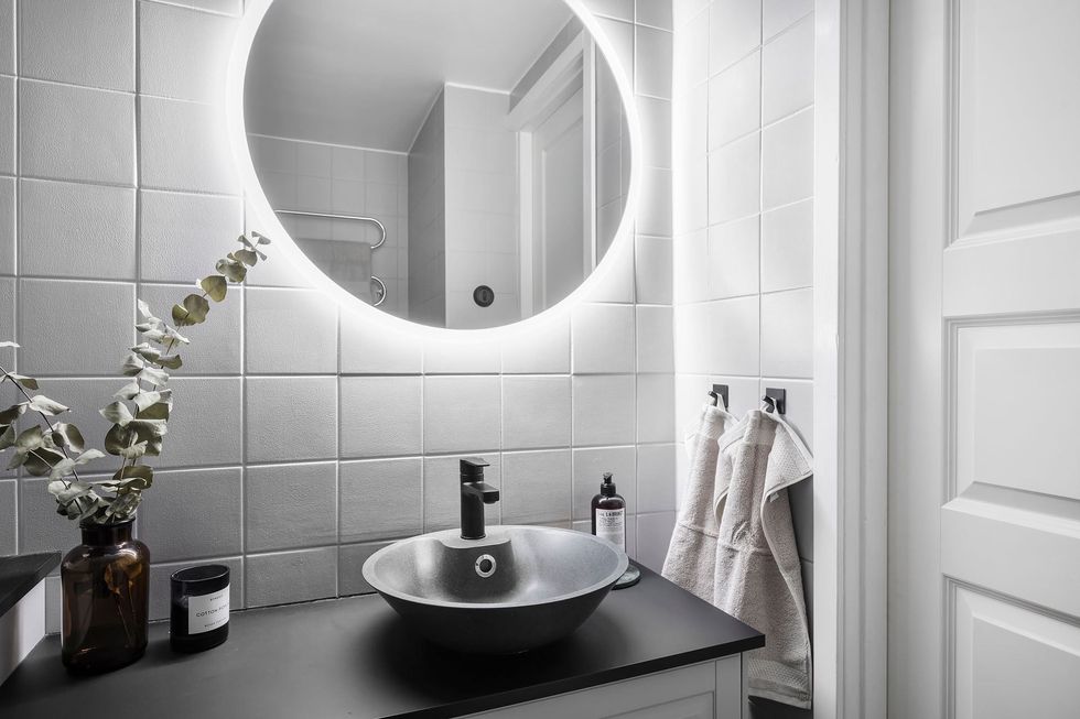 baño moderno con azulejos blancos, espejo redondo y encimera negra