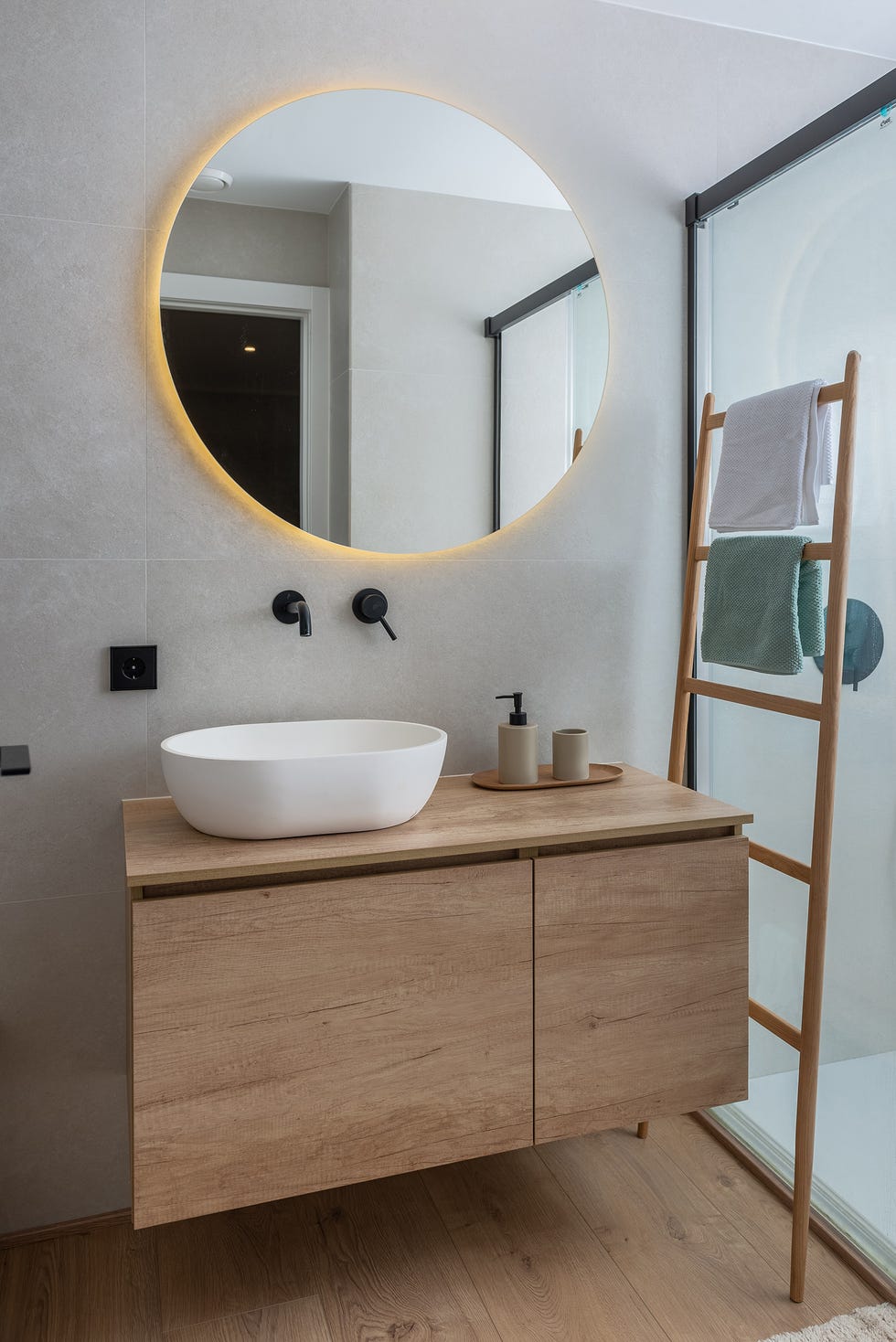 baño con mueble de madera volado y espejo redondo