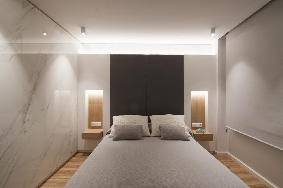 dormitorio con hornacinas de madera y mesitas de noche suspendidas, y paredes revestidas con efecto mármol