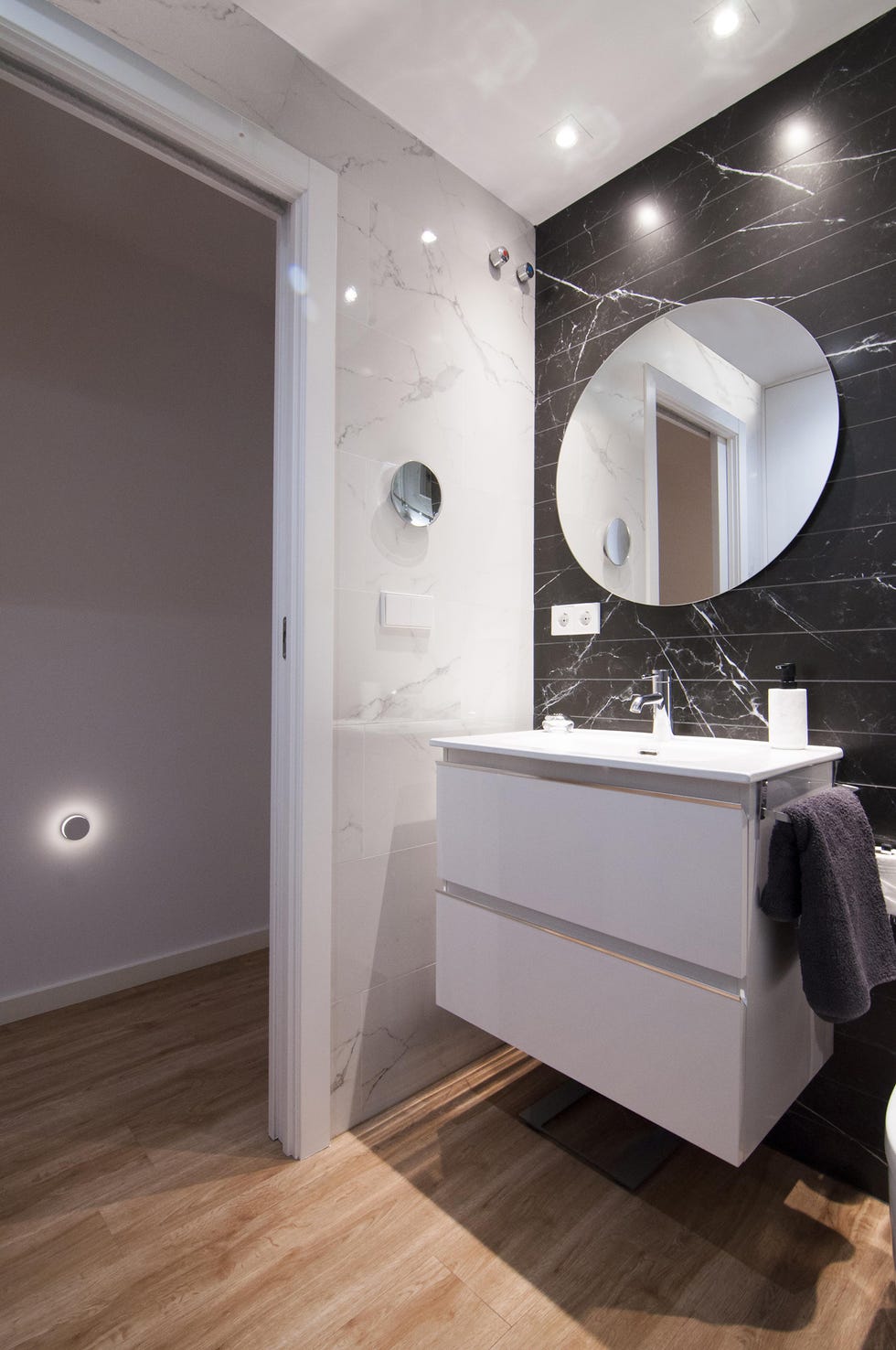 baño con mueble de lavabo suspendido en blanco y pared revestida con efecto mármol negro