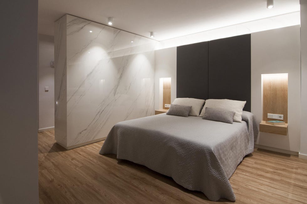 dormitorio con hornacinas de madera y mesitas de noche suspendidas, y paredes revestidas con efecto mármol