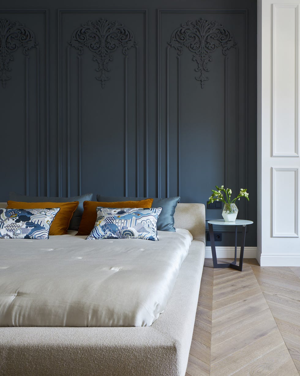 dormitorio de estilo parisino con molduras decorativas en la pared del cabecero y parquet en espiga