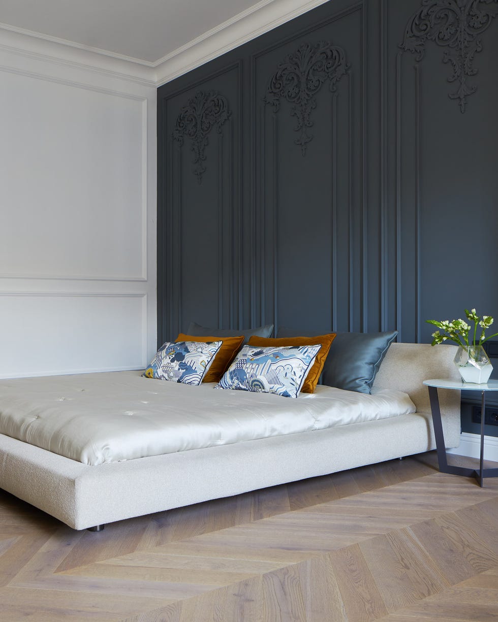 dormitorio de estilo parisino con molduras decorativas en la pared del cabecero y parquet en espiga