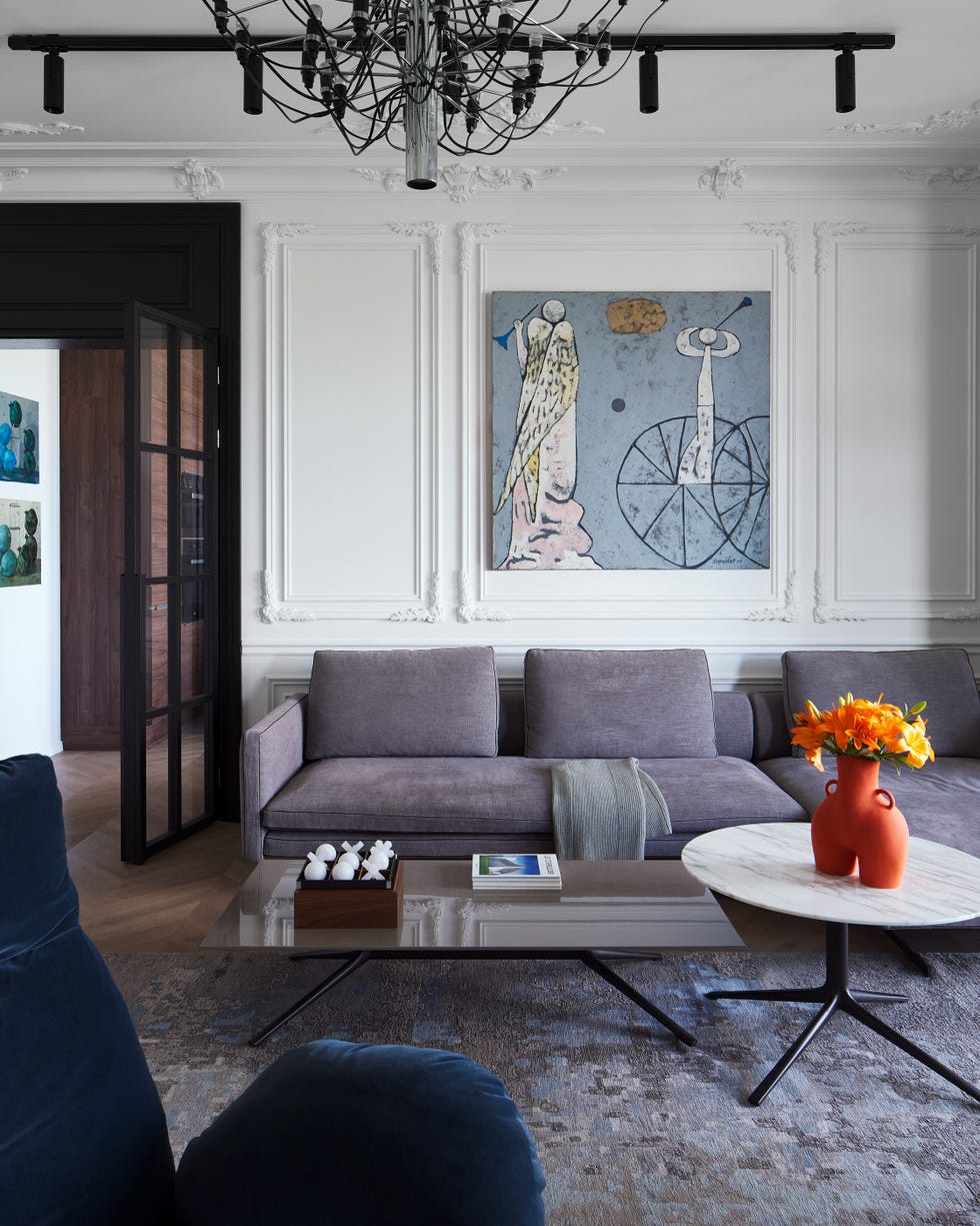 salón con molduras decorativas en las paredes, sofá gris de terciopelo, mesa de centro baja con sobre rectangular y mesa auxiliar con sobre redondo de mármol