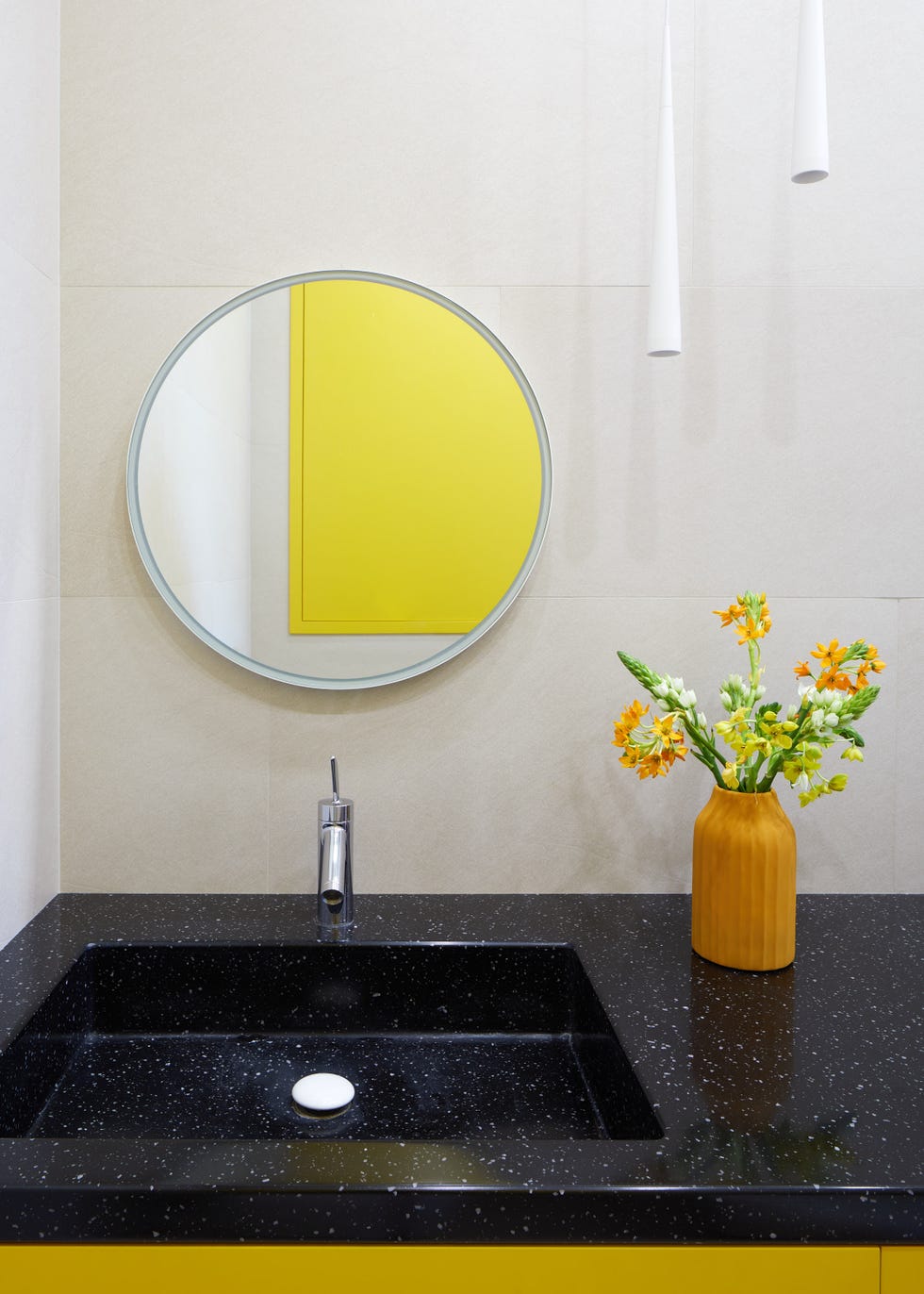 baño con encimera de granito negro y mueble amarillo, espejo redondo y lámparas suspendidas de diseño moderno