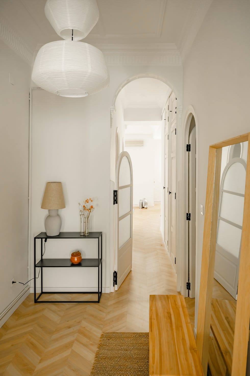 recibidor con suelo de parquet en espiga, techo con molduras, puertas con arcos y consola de metal negro