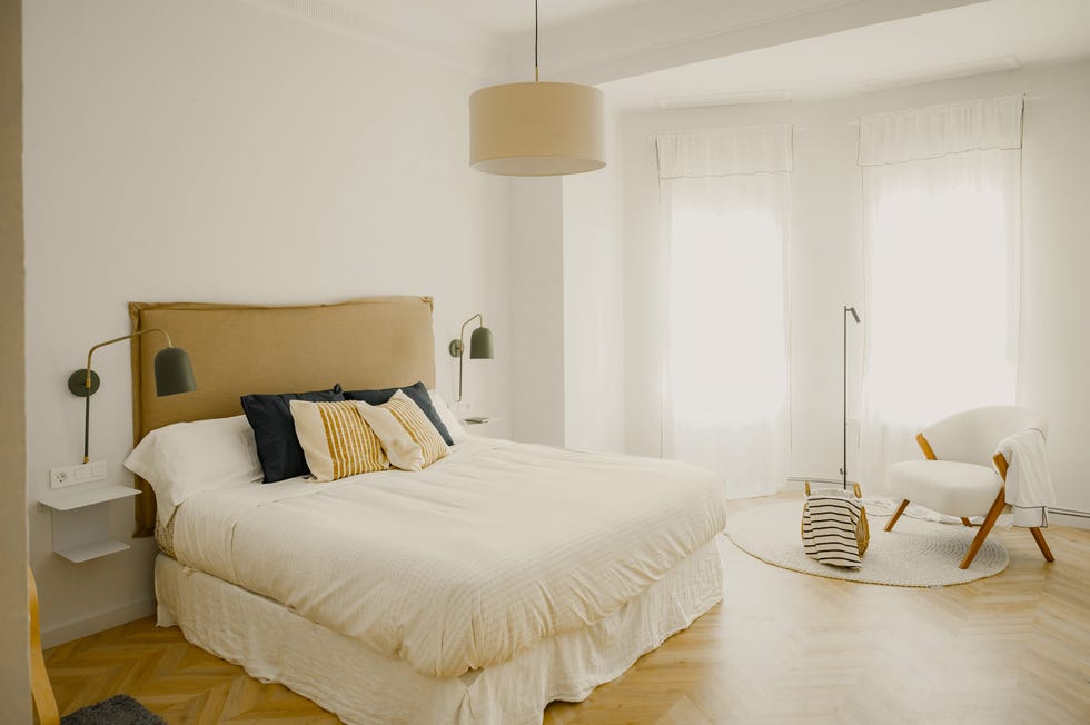dormitorio minimalista con cabecero de lino y rincón de lectura con butaca blanca