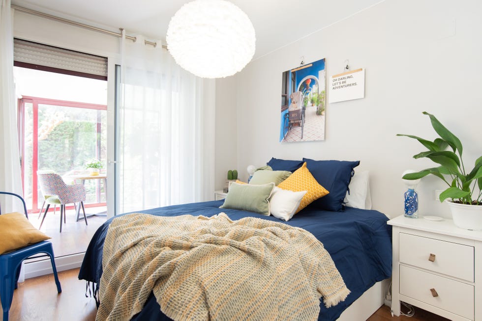 dormitorio moderno con el mobiliario y la pared de color blanco, ropa de cama azul y acceso a la terraza
