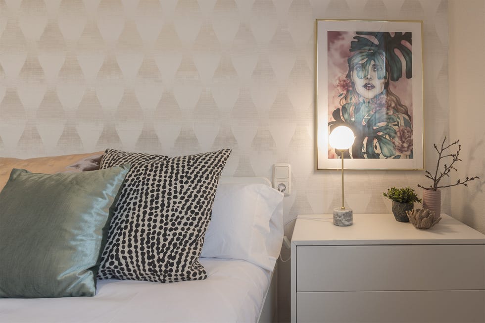 dormitorio con papel pintado con motivos geométricos y mesilla de noche blanca