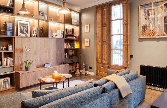 salón con estantería a medida en madera, contraventanas de madera y sofá gris