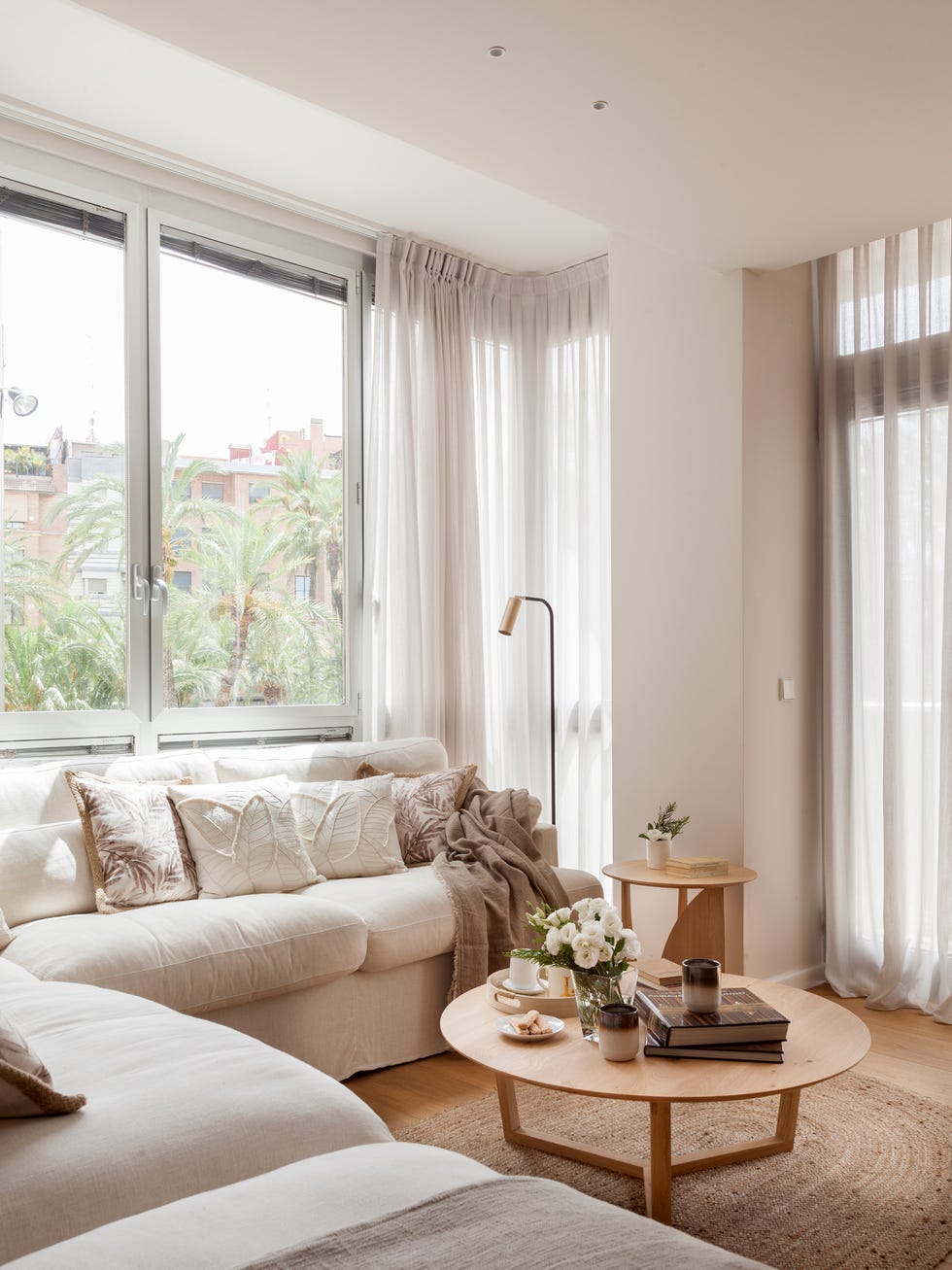 sofá rinconera blanco y mesa de centro redonda de madera a juego con la auxiliar