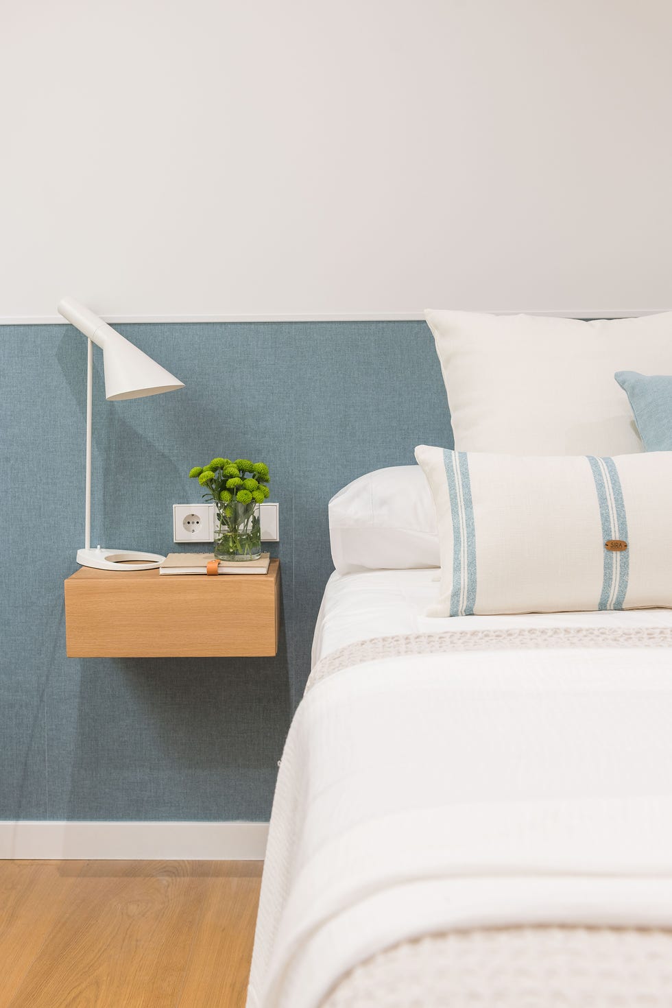 dormitorio con papel pintado azul en el cabecero y mesita de madera volada