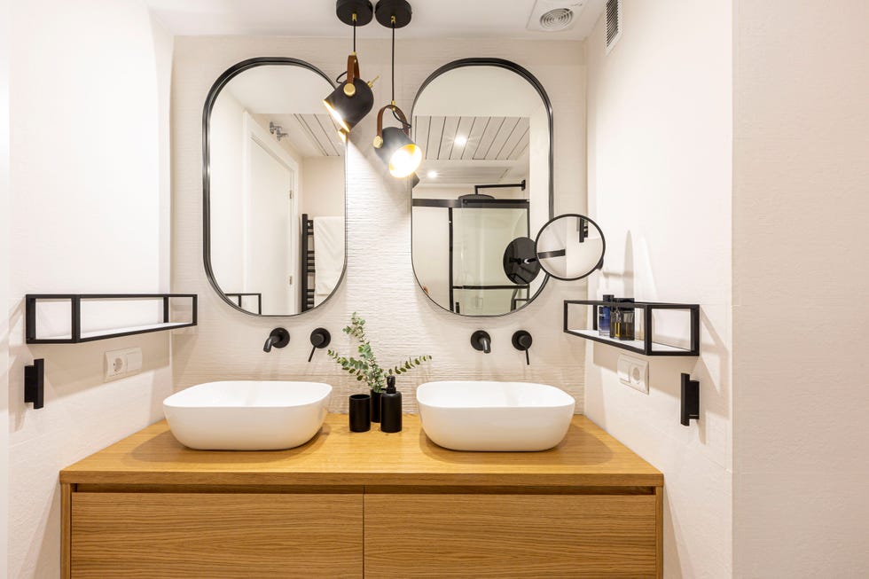 baño con mueble de madera suspendido y dos espejos ovalados con marco negro