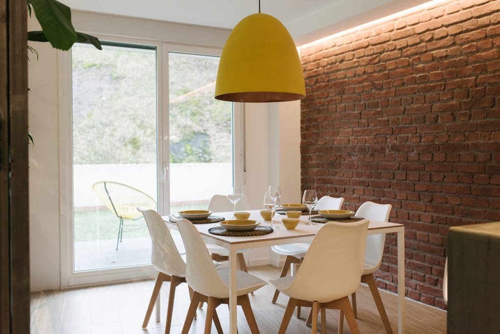 comedor de diseño nórdico con mesa y sillas blancas y pared de ladrillo visto