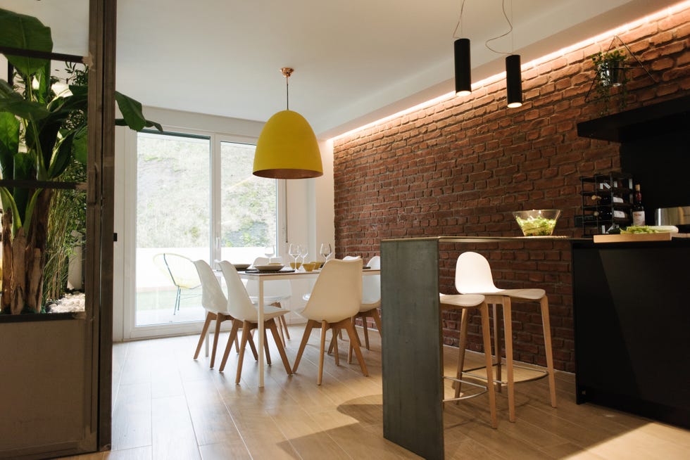 comedor de diseño nórdico con mesa y sillas blancas y pared de ladrillo visto