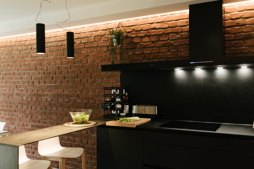 cocina de color negro con península y pared de ladrillo visto