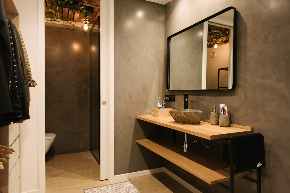 baño en suite con paredes de microcemento gris y baldas flotantes de madera
