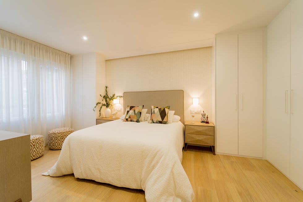 dormitorio con armario blanco empotrado, mesillas de madera y cama con cabecero tapizado en beige