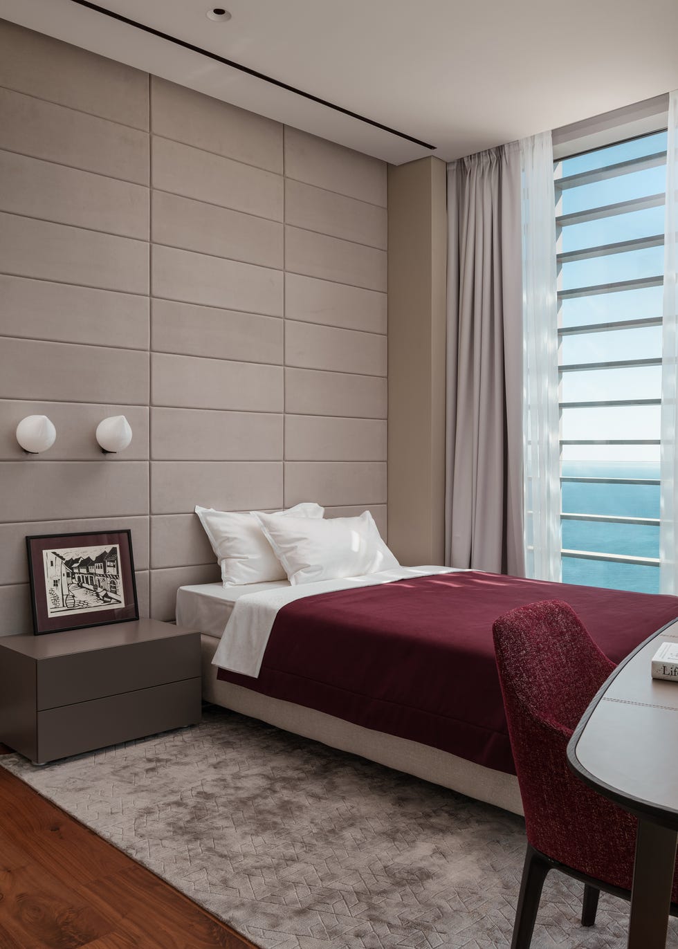 dormitorio con pared acolchada en color beige y textiles burdeos