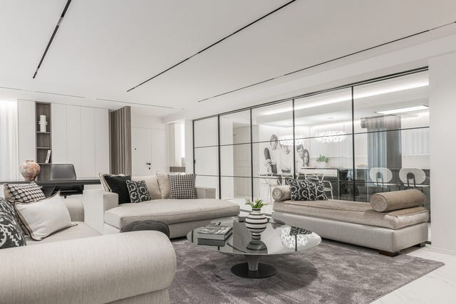 salón comedor con sofás en tonos grises y cocina con cristalera