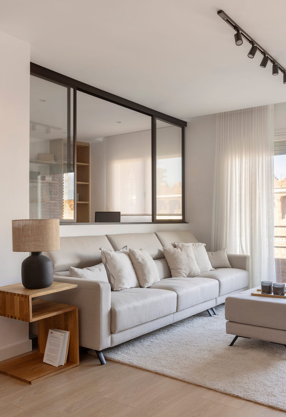 sofá beige, mesa auxiliar de madera y cerramiento de cristal