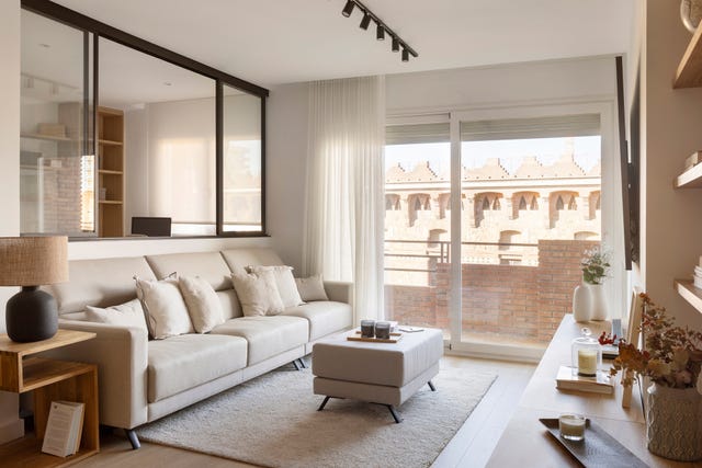 salón con cerramiento de cristal y sofá beige junto a mesa auxiliar de madera