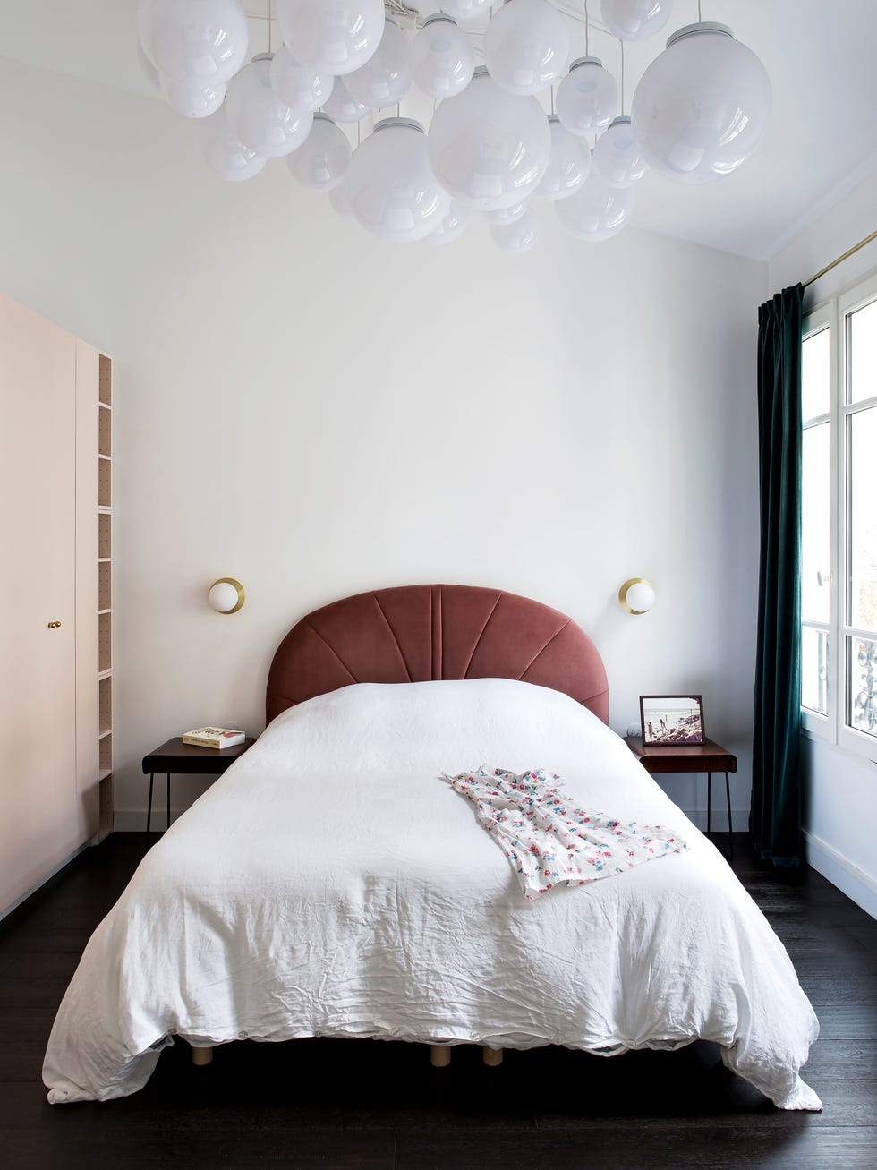 dormitorio con cama con cabecero de terciopelo granate, armario de color rosa pastel y lámparas de techo tipo bola