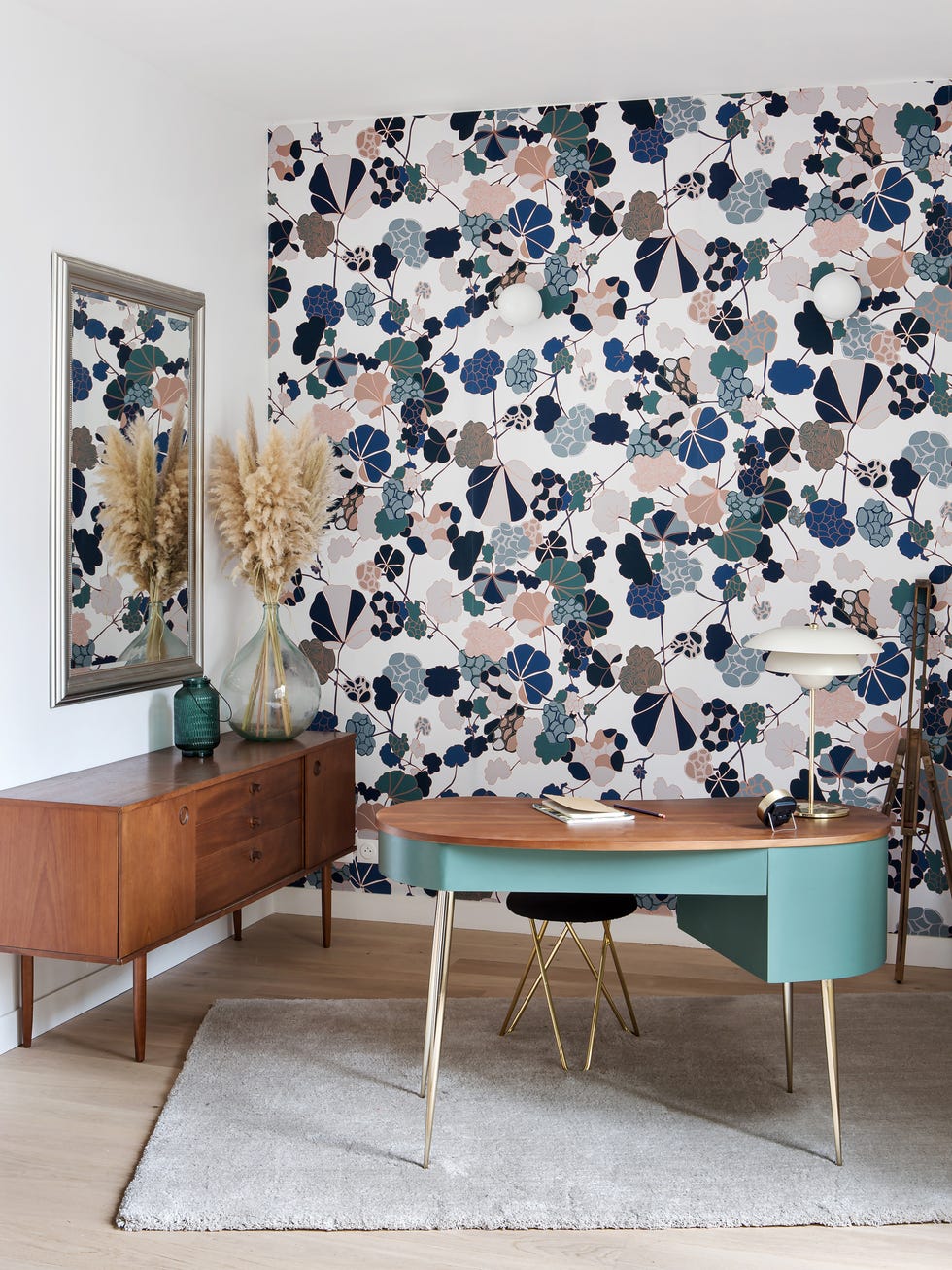 despacho de diseño mid century con papel pintado floral en la pared y escritorio verde con patas doradas