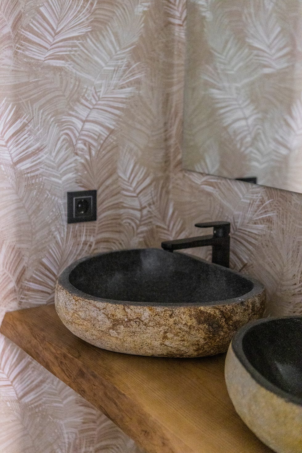 baño con papel pintado botánico, encimera de madera y lavabos de piedra