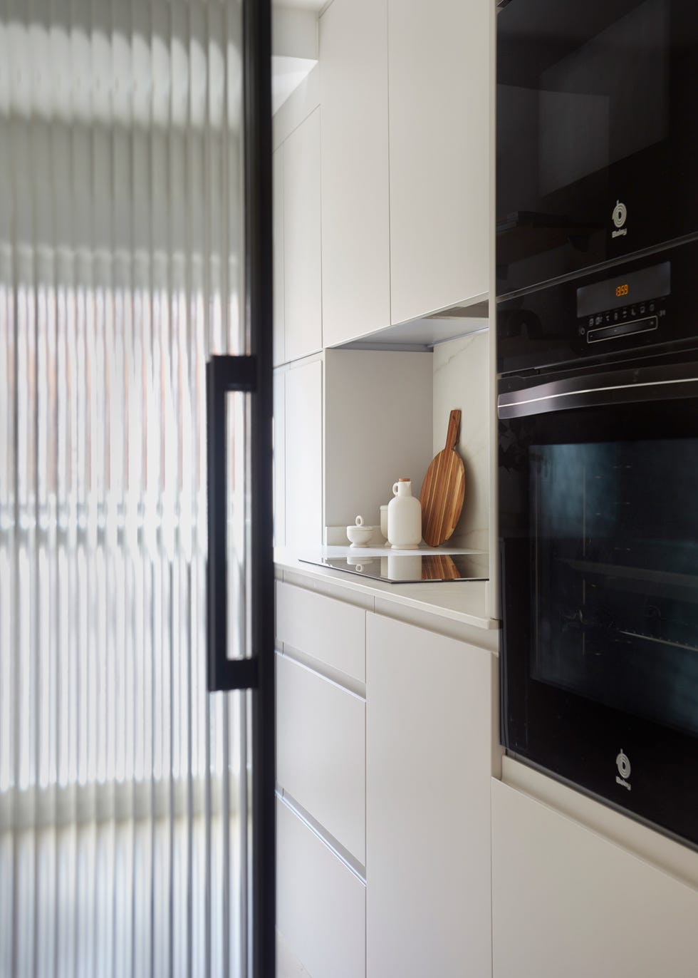 cocina blanca moderna con frentes lisos y puerta de vidrio con perfil de metal negro