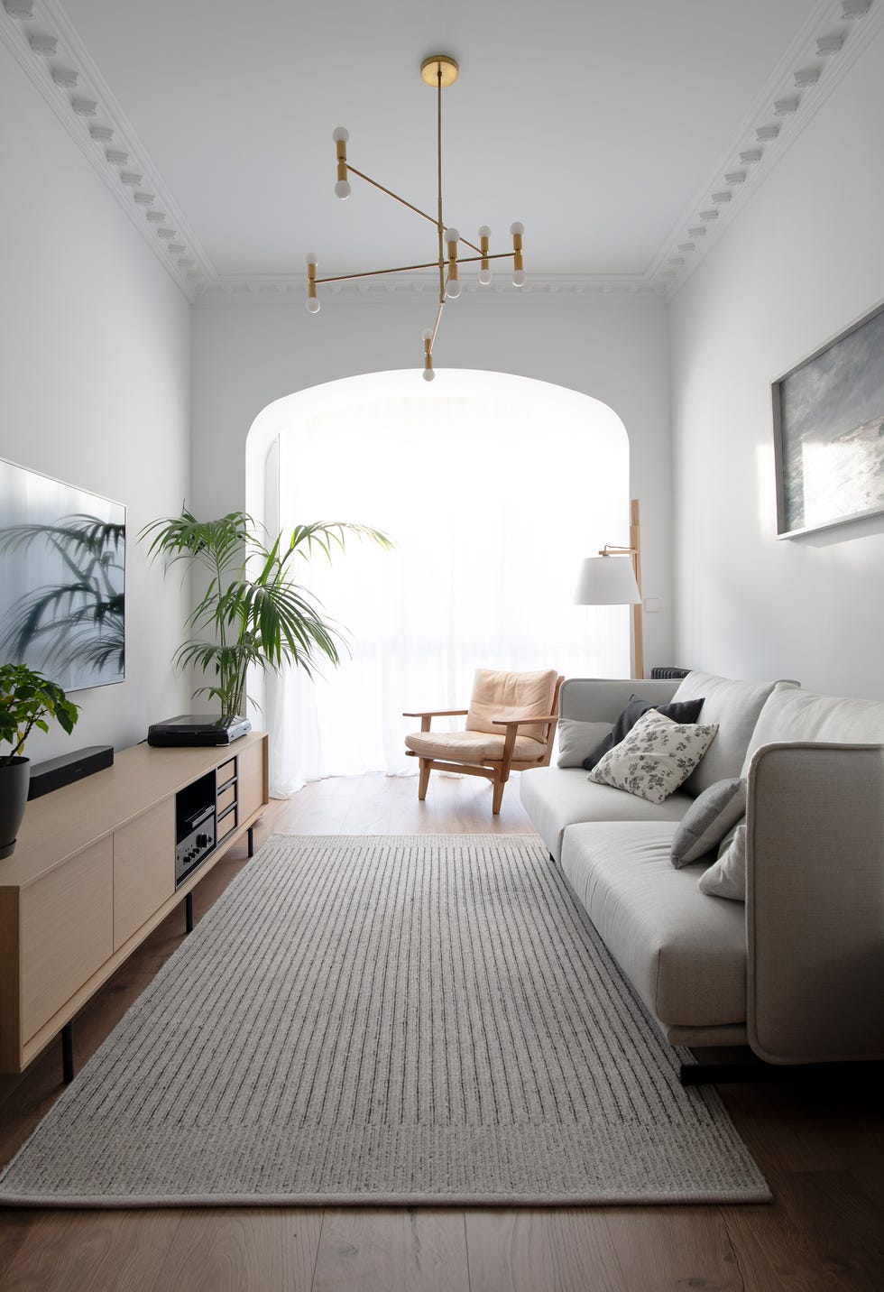 salón moderno con sofá gris, butaca de madera, mueble tv de madera y lámpara dorada mid century