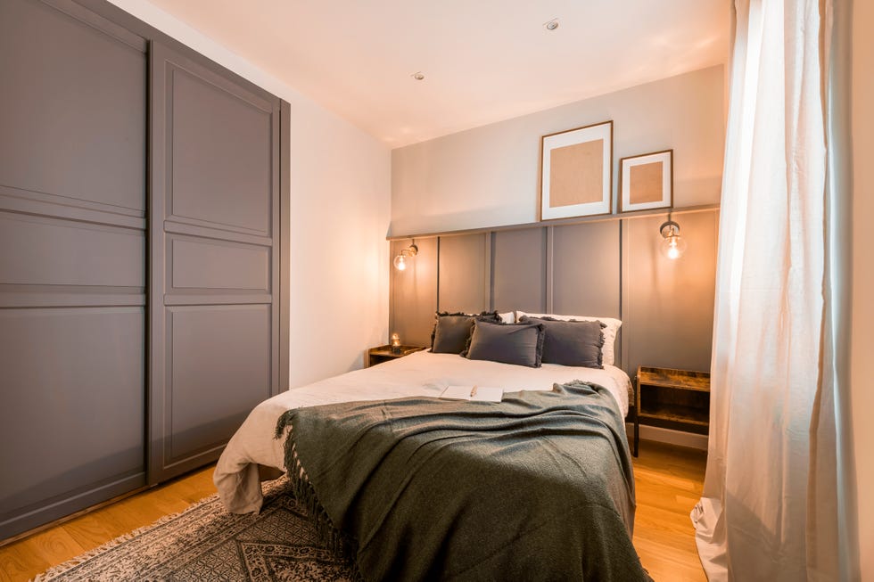 dormitorio con arrimadero con molduras decorativas en color gris como cabecero y armario a juego