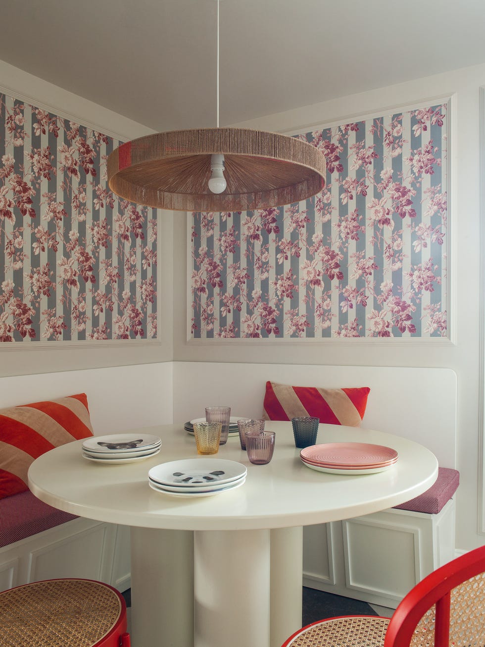 office en esquina con mesa de comedor blanca redonda, sillas rojas, banco y papel pintado enmarcado con molduras
