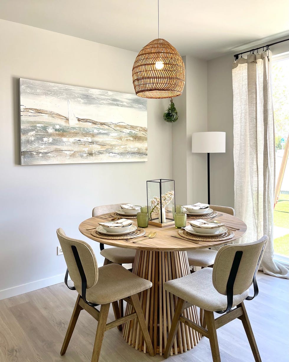 mesa de comedor de madera redonda, sillas tapizadas en beige y lámpara de fibras