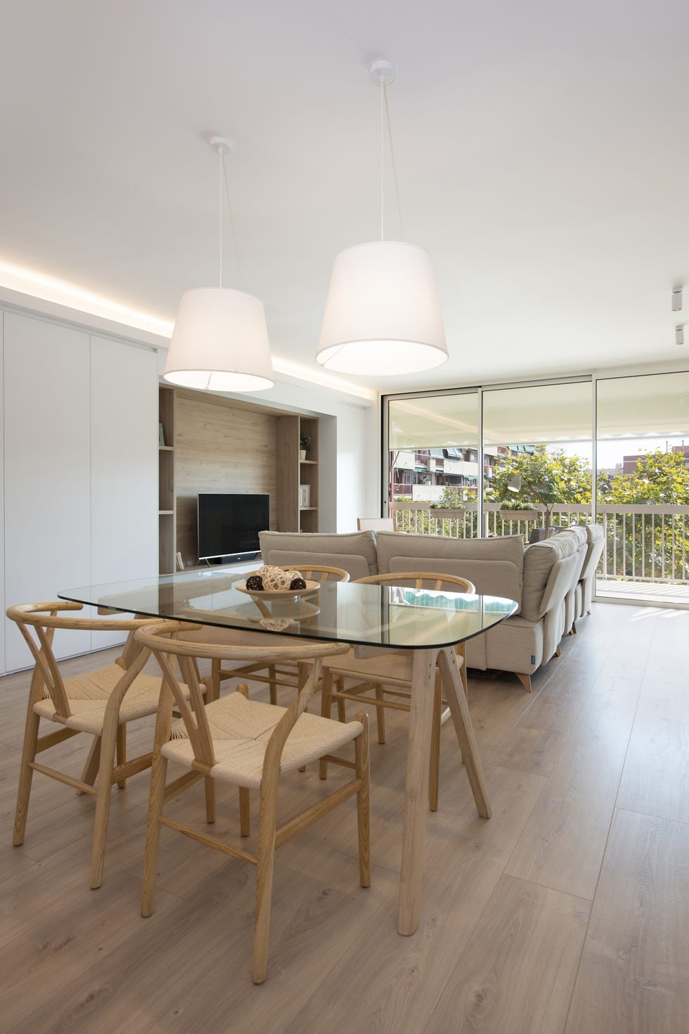 comedor con mesa de madera y cristal, sillas wishbone y lámpara de techo blanca