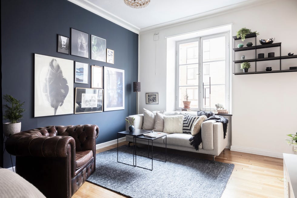 salón de estilo nórdico con pared de color azul marino butaca tipo chester de cuero marrón y sofá gris