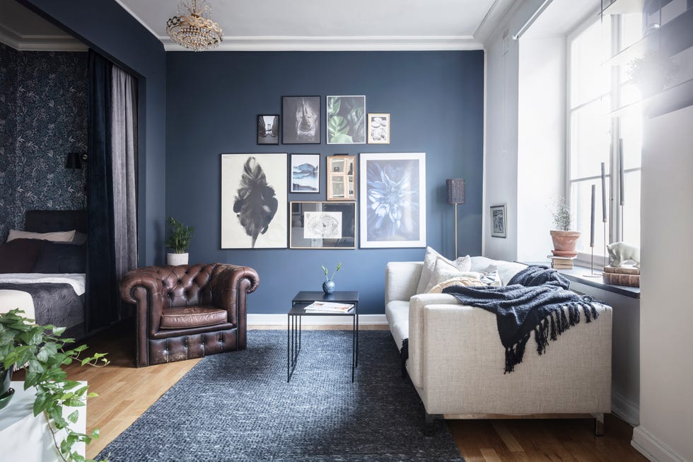 salón de estilo nórdico con pared de color azul marino butaca tipo chester de cuero marrón y sofá gris